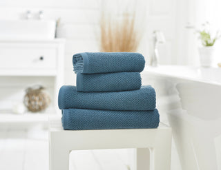 Stack of blue towels on a white surface with a blurred bathroom background